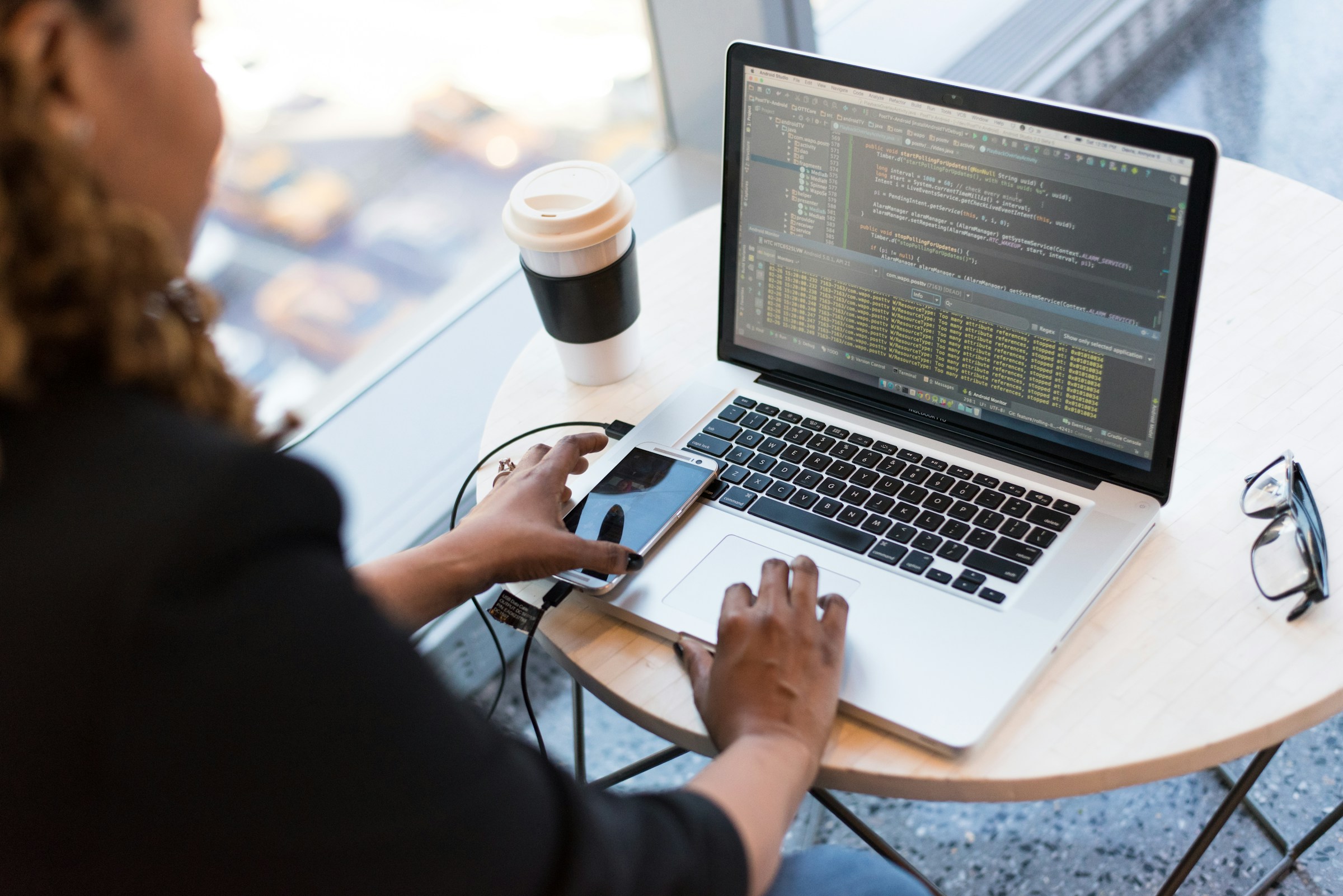 A developer writing code in Android Studio on a laptop at a café table